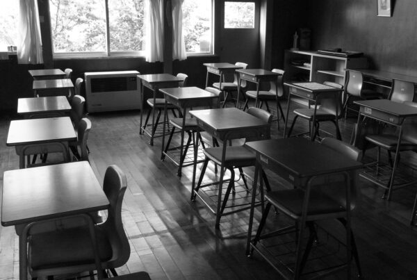 Black and white photo of desks and chairs in an empty classroom.